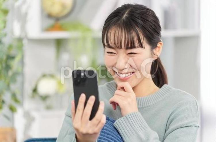 ソファに座ってスマートフォンを見る女性 女性,スマートフォン,ソファの写真素材