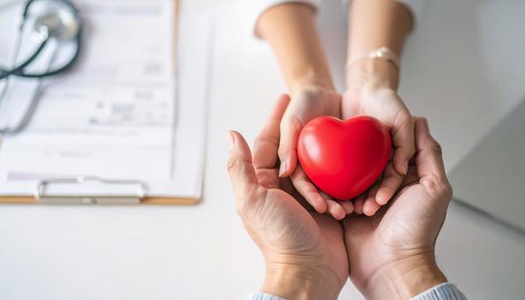 ハートを贈る　机の上でハートを握る両手の写真