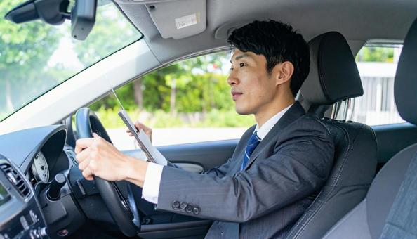 手もとに書類を持って運転するサラリーマン 手もとに書類を持って運転するサラリーマンの写真
