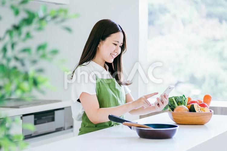 スマホを見ながら料理する女性（笑顔） 料理,家事,スマホの写真素材