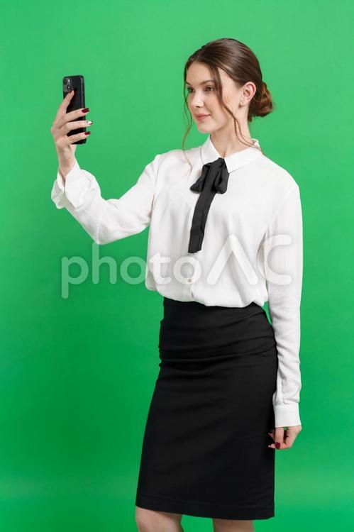 スマホを見るお団子ヘア女性（緑背景） 女性,スマートフォン,持つの写真素材