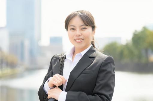 ビル街でカメラ目線のスーツの女性 ビル街でカメラ目線のスーツの女性 日本人,女性,20代の写真素材