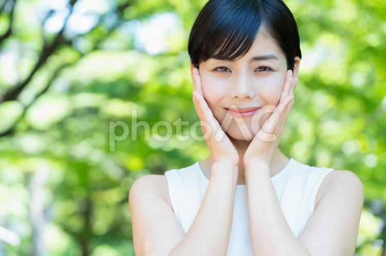 緑の中でスキンケアをする若い女性 スキンケア,ビューティー,女性の写真素材