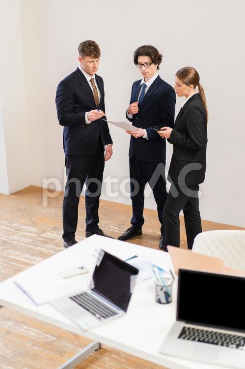 机の傍に立ち話している男女 男女,打ち合わせ,立ち話の写真素材