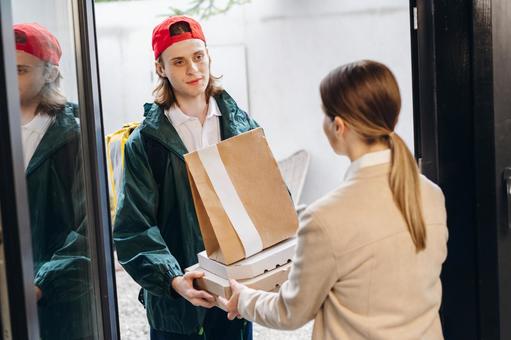 玄関で紙袋とピザ箱を女性に渡す配達員の男性 配達,フードデリバリー,デリバリーの写真素材