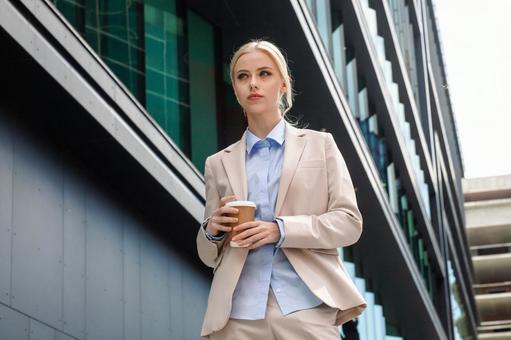 オフィスビルの外でコーヒーを持って立っている外国人女性 ビジネスウーマン,ビジネス,女性の写真素材