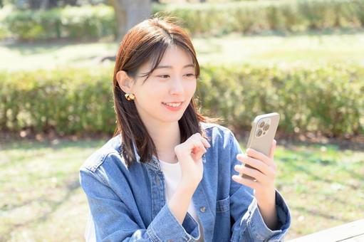 公園でスマホを操作する日本人女性 公園でスマホを操作する日本人女性 女性,スマホ,スマートフォンの写真素材