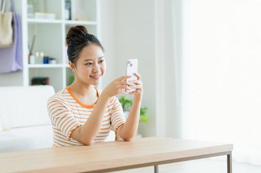 リビングでスマホを見る若い女性 リビングでスマホを見る若い女性の写真