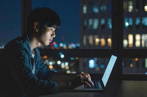 夜のカフェでパソコンで作業する男性の写真