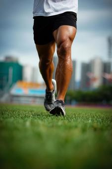 芝生の上を走るマッチョな男性の足元の写真