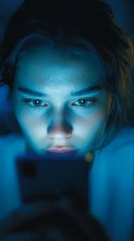 暗闇でスマートフォンを見つめる女性の顔の写真