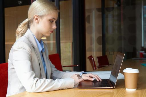 オフィスのテーブルでノートパソコンを使っているビジネスウーマンの写真