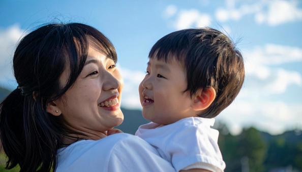青空の下、子供を抱っこする母親 青空の下、子供を抱っこする母親の写真