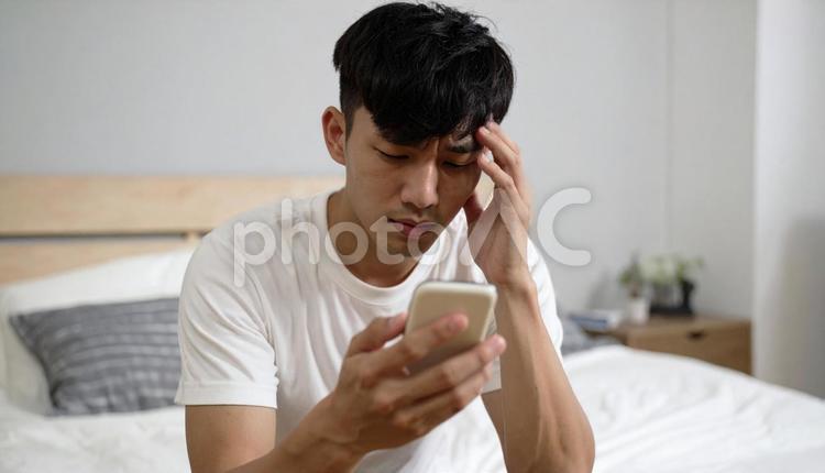 スマートフォンを見て悩む室内ポートレート 人物,男性,若者の写真素材