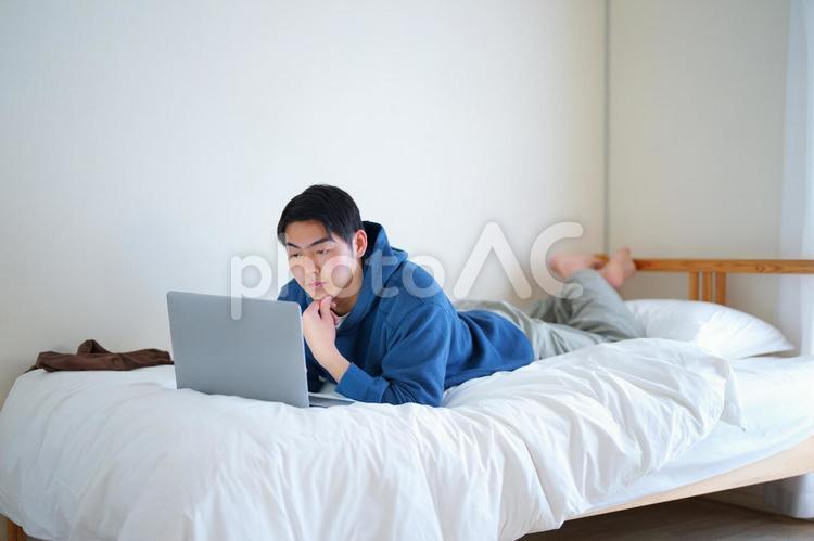 ベッドで腹ばいでノートパソコンを使っている男性 引っ越し,一人暮らし,男性の写真素材