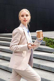 コーヒーとスマートフォンを持ってオフィスビルの外の階段を登るビジネスウーマン ビジネスウーマン,ビジネス,女性の写真素材