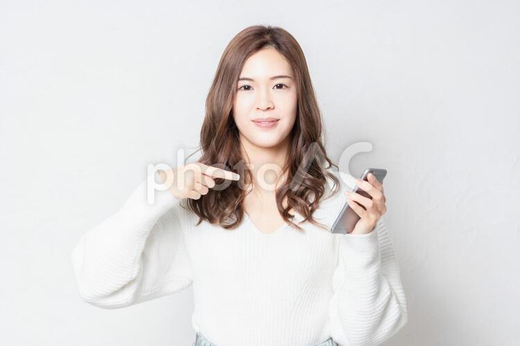 白い壁の前に立って、スマホを使う若い女性 女性,スマホ,snsの写真素材
