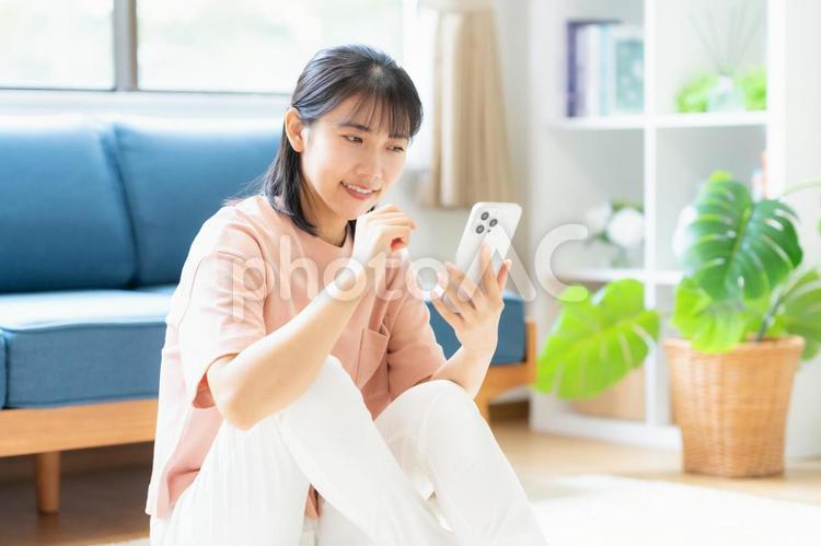 リビングでスマホを見る大学生の女性 女性,スマホ,大学生の写真素材