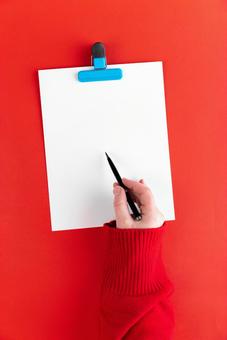 水色のクリップで挟まれた白い紙にボールペンで書く手(赤背景) 水色のクリップで挟まれた白い紙にボールペンで書く手(赤背景) モックアップ,女性,手の写真素材
