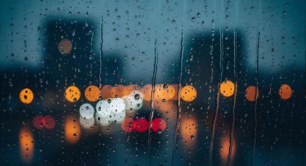 雨に濡れる窓越しにぼやける街の光の写真