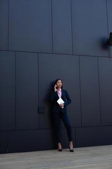 オフィスビルの黒い壁の前で電話するパンツスーツのアジア人ビジネスウーマン ビジネスウーマン,ビジネス,女性の写真素材