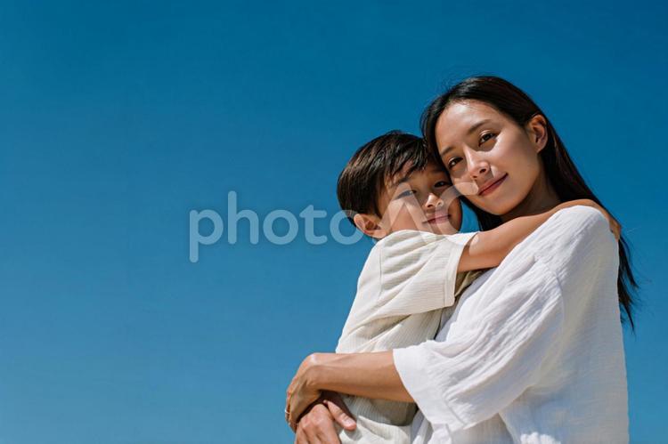 青空の下で息子を抱きしめる母 親子,家族,母親の写真素材