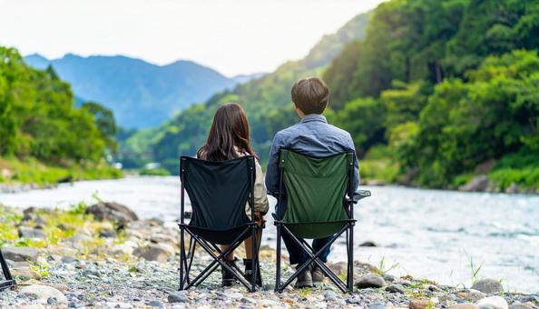 椅子に座って二人並んで川を眺める若い男女 椅子に座って二人並んで川を眺める若い男女の写真