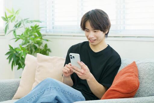 ソファでスマホを操作する若い日本人男性 男性,若い,スマートフォンの写真素材