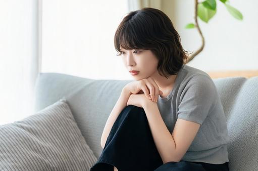 リビングのソファに座って考える女性 リビングのソファに座って考える女性 女性,考える,困るの写真素材
