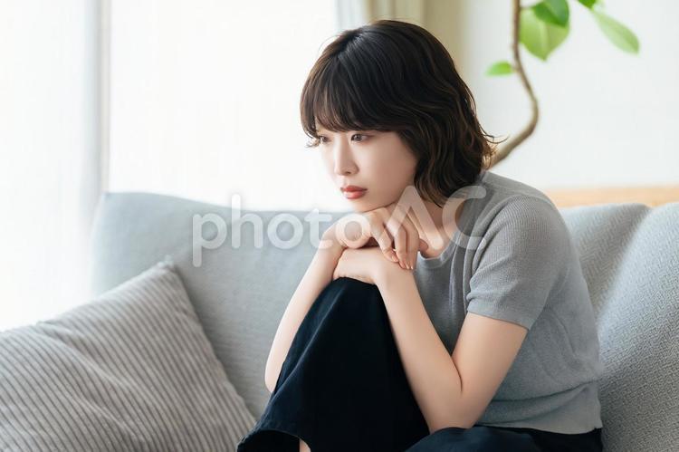 リビングのソファに座って考える女性 リビングのソファに座って考える女性 女性,考える,困るの写真素材