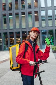 街なかでスマートフォンの画面を見せるフードデリバリーの男性 配達,フードデリバリー,デリバリーの写真素材