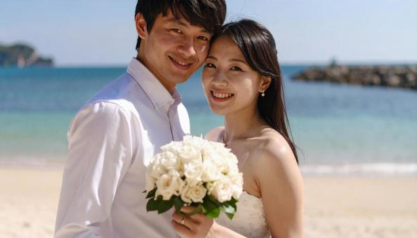海辺でブーケを持ち顔を見合わせる新郎新婦 海辺でブーケを持ち顔を見合わせる新郎新婦の写真