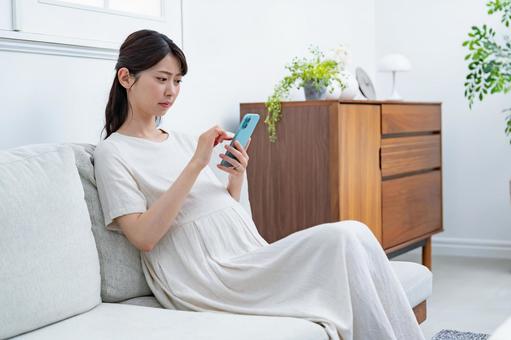 ソファで携帯を持つ女性 悩む,妊婦,妊娠の写真素材