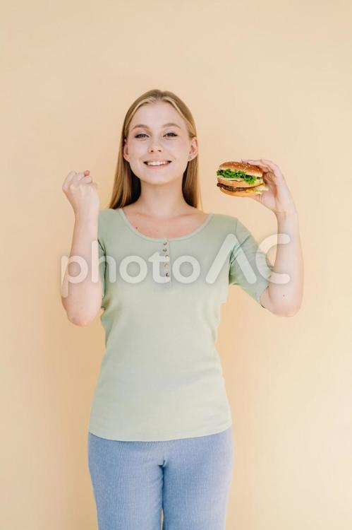 カメラ目線でガッツポーズしてハンバーガーを持っている女性 女性,人物,ハンバーガーの写真素材