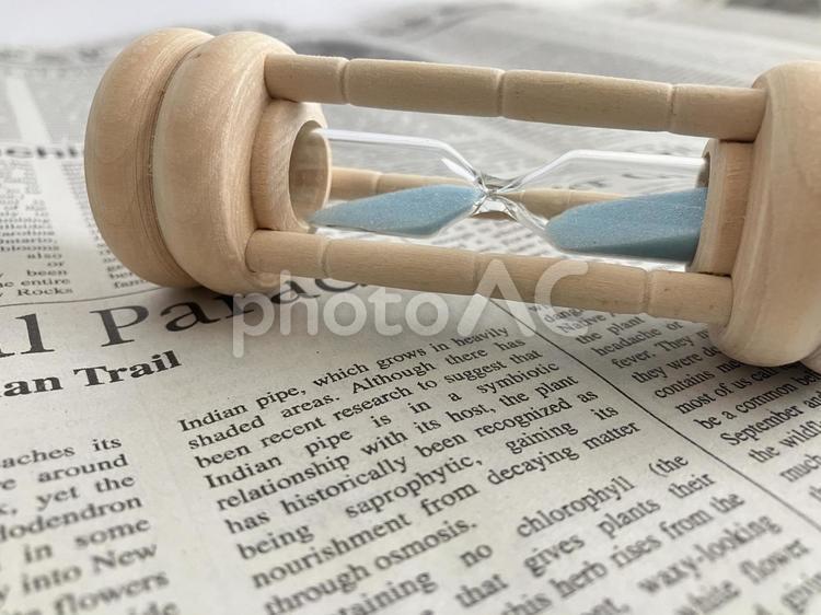 英字新聞の上で倒れた砂時計 英字新聞,砂時計,時計の写真素材