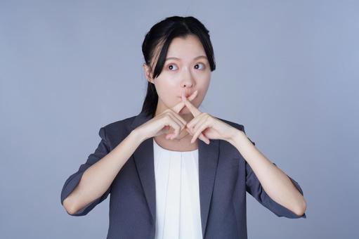 口元でバツ印を作るスーツを着た女性の写真