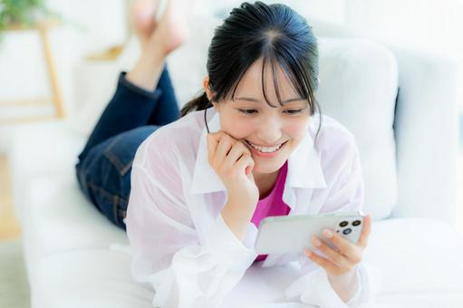 部屋でスマホを操作する若い女性 部屋でスマホを操作する若い女性 スマホ,若い女性,笑顔の写真素材
