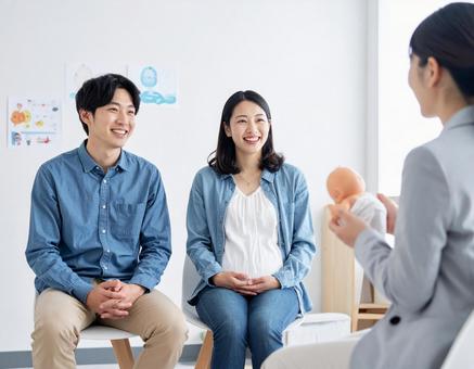 新米パパ、ママ教室で育児を学ぶ若い夫婦の写真