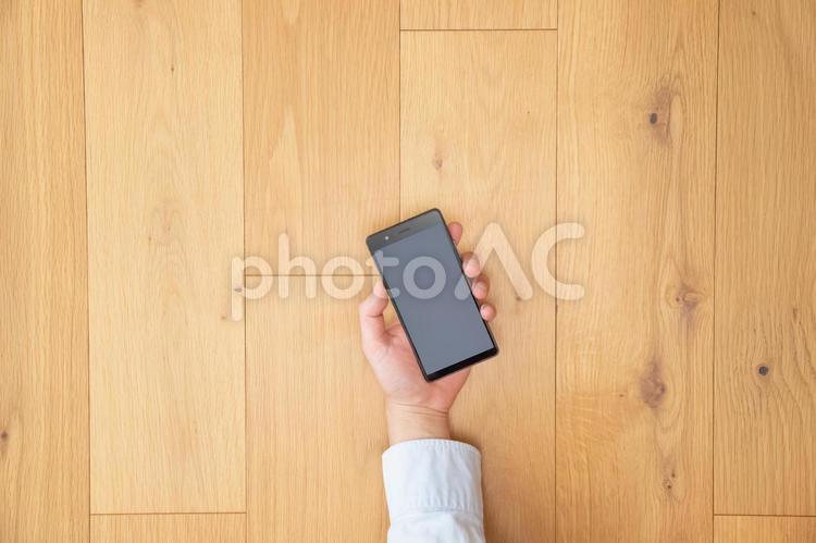 スマホを手にする男性の手-茶色の木目デスク ビジネス,男性,日本人の写真素材