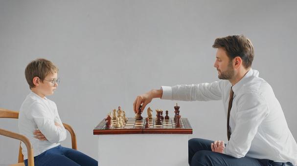 向かい合ってチェスをする横向きの親子(グレー背景) 向かい合ってチェスをする横向きの親子(グレー背景) チェス,親子,お父さんの写真素材