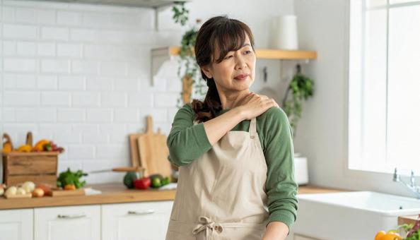 キッチンで肩こりを感じるエプロン姿の女性 キッチンで肩こりを感じるエプロン姿の女性の写真