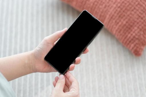 リビングでスマホを持っている女性の手元 リビングでスマホを持っている女性の手元 スマホ,部屋,手の写真素材