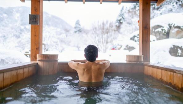 雪山の露天風呂に浸かる男性の後ろ姿 雪山の露天風呂に浸かる男性の後ろ姿の写真