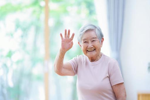 右手をあげカメラ目線のおばあちゃん 女性,手を挙げる,手を振るの写真素材