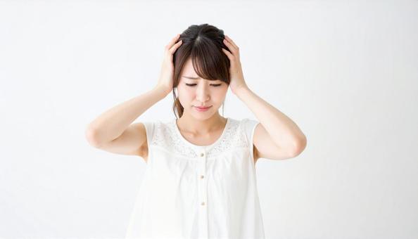頭を押さえて辛そうな表情をする女性 頭を押さえて辛そうな表情をする女性の写真