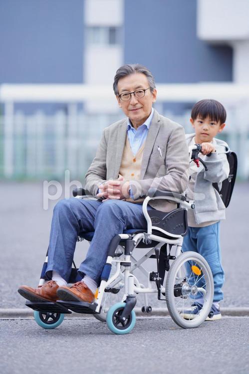 祖父の乗った車椅子を押すランドセルを背負った男の子 男の子,小学生,子どもの写真素材