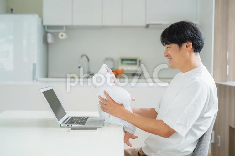 赤ちゃんを抱きながら仕事する男性 テレワーク,育児,リモートワークの写真素材