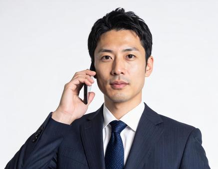 携帯電話で通話するビジネスマンの正面 携帯電話で通話するビジネスマンの正面の写真