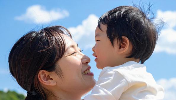 青空の下、子供を抱っこする母親 青空の下、子供を抱っこする母親の写真