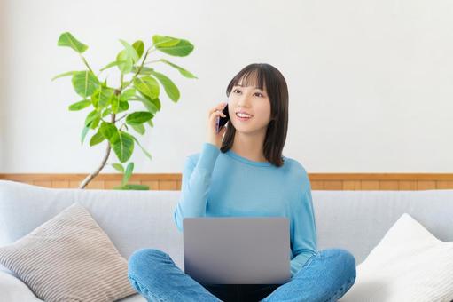 ソファに座ってスマホとパソコンを使う女性 女性,パソコン,スマホの写真素材